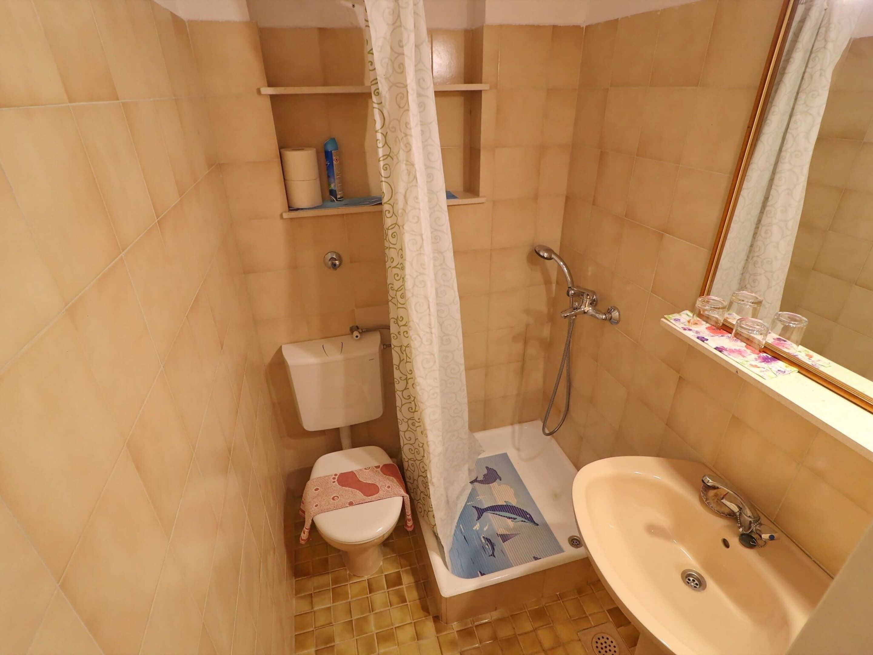 Un baño con inodoro, ducha, lavabo y repisas con artículos de aseo.
