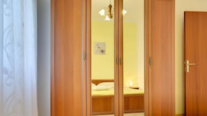 Une chambre à coucher avec une armoire en bois, un lit recouvert d’une couvre-lit jaune et une table de chevet avec une lampe.