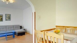 Un salon chaleureux avec un canapé, une table basse bleue et un coin repas comprenant des chaises en bois et une table dressée avec des fruits.