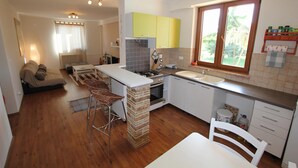 A compact kitchen with a central island, a dining area with a table and chairs, and a living area with a sofa and a TV. - Apartment in Fazana With Garden & Terrace (Fazana)