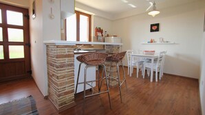 A kitchen with a brick island, white bar stools, a dining table with chairs, and a hanging light fixture. - Apartment in Fazana With Garden & Terrace (Fazana)