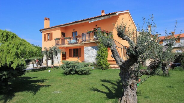 A two-story house with a balcony, surrounded by a well-maintained lawn and trees. - Apartment in Fazana With Garden & Terrace (Fazana)