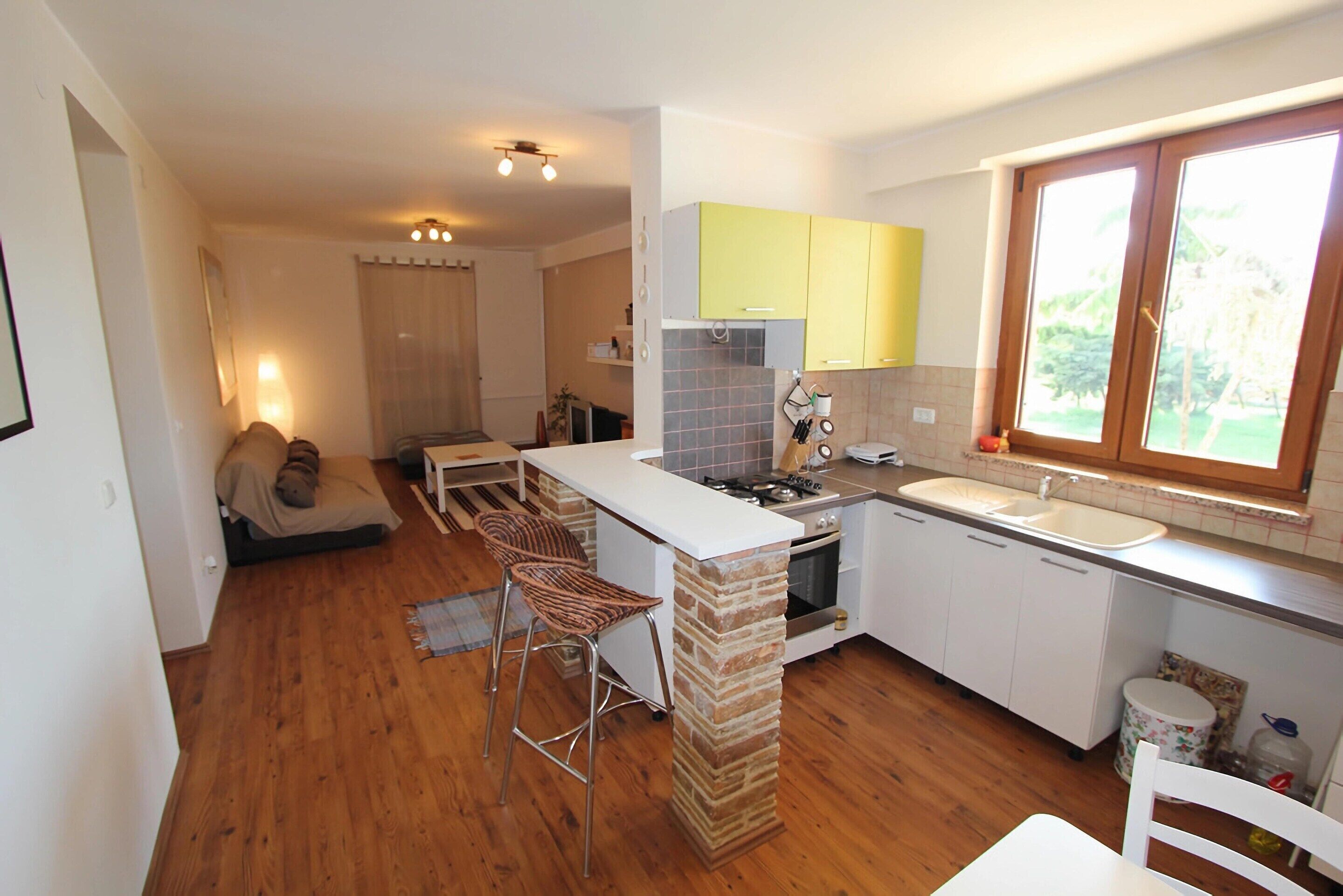 A compact kitchen with a central island, a dining area with a chair, and a window providing natural light.