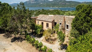 Un edificio rústico de piedra con techo de tejas, rodeado de abundante vegetación y un paisaje montañoso.