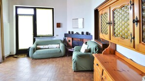Ein gemütliches Wohnzimmer mit Holzboden, Kamin, einem grünen Sofa und einem Holzschrank.