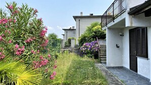 Ein Innenhof mit einem gepflasterten Weg, einem weißen Gebäude mit Balkon und verschiedenen blühenden Pflanzen.