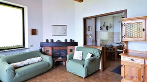 Ein Wohnzimmer mit Kamin, grünen Sofas, einem Holzkabinett und einem Essbereich.