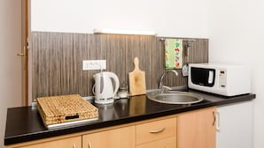 A small kitchenette with a microwave, kettle, and wooden cutting board on the counter.