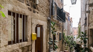 A narrow street with stone buildings, a wooden door, and potted plants.