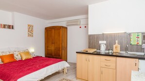 A bedroom with a bed, a wardrobe, and a kitchenette with a sink and a kettle.