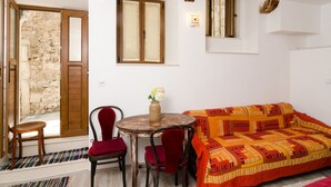 A cozy room with a wooden door, a small table with chairs, a colorful sofa, and a window with curtains.