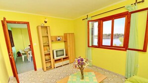 A room with yellow walls, a wooden TV stand, a table with a vase of flowers, and a window with a view of a lake. - Apartments Bacic - Three Bedroom Apartment With Terrace and Sea View (Blato)