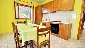 A compact kitchen with wooden cabinets, a tiled backsplash, and a dining table set with chairs. - Apartments Bacic - Three Bedroom Apartment With Terrace and Sea View (Blato)