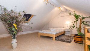 Ein Schlafzimmer mit schrägem Dach, einem Bett, einem Nachttisch, einer Lampe, einem Topfpflanzen und einer dekorativen Pfauenfeder-Anordnung.