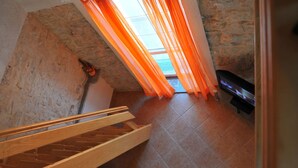 Eine Treppe führt zu einem Erkerbereich mit Steinwand, Holzbalken und orangefarbenen Vorhängen.