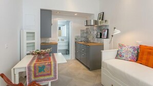 Ett kompakt bostadsutrymme med en matplats, ett litet kök och en soffa med en färgglad kudde.