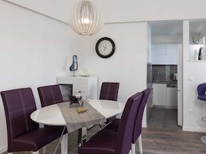 A modern dining area with a round table, purple upholstered chairs, a decorative clock, and a pendant light.