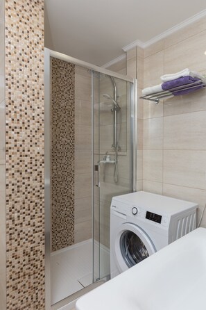 A modern bathroom with a glass-enclosed shower, a washing machine, and a tiled wall with a mosaic pattern.