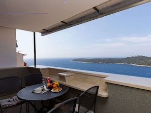 A balcony with a table set for two, overlooking a coastal view with a distant island.