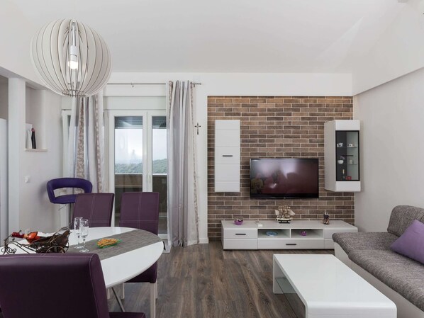 A modern living room with a TV, white cabinets, and a brick wall.