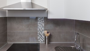 Una cocina moderna con campana de acero inoxidable, un respingo con mosaicos y un lavamanos de acero inoxidable con grifo.