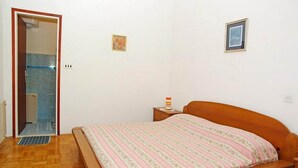 Un dormitorio con cama de madera, una mesita de noche, una alfombra pequeña y una puerta que da a un baño.