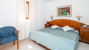 A bedroom with a bed, a chair, a window with curtains, a painting on the wall, and two bedside lamps. - Apartments Lion - Sea House 1 (Dubrovnik)