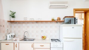 A compact kitchen with a gas stove, a sink, and a microwave. There is a small refrigerator and a shelf with kitchen items. - Apartments Lion - Sea House 1 (Dubrovnik)