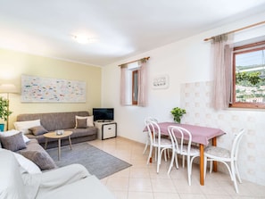 Ein Wohnzimmer mit einer Couch, einem Couchtisch, einem Fernseher und einem Essbereich mit Stühlen und Tisch.