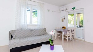 A modern room with a sofa, a small table with a potted plant, and a dining area with chairs and a table. - Apartments Kola's Mill - Comfort One Bedroom Apartment With Terrace and Sea View (Dubrovacko Primorje)