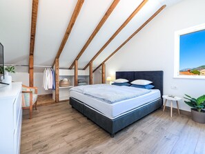 A bedroom with a bed, wooden beams, a desk, a chair, a small table, and a potted plant. - Apartments Terra - One Bedroom Apartment With Balcony and Garden View (Dubrovnik)