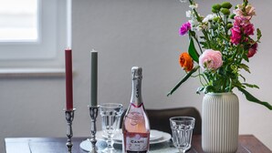Een eettafel gedekt met borden, bestek, een fles Canti Rose, kaarsen en een vaas met bloemen.