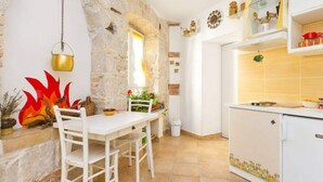 Una cocina con armarios blancos, encimera blanca y pared de piedra. Se ve una ventana con vistas al exterior y una olla colgando.