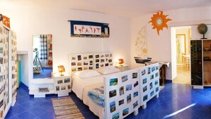 Un dormitorio con una cama cubierta de fotografías, un escritorio con una lámpara y un adorno de sol en la pared.