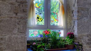 Una ventana con vidrieras que representan pájaros y flores, rodeada de plantas en macetas.