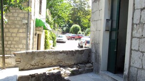 Unos escalones de piedra conducen a la entrada de un edificio con una puerta verde, rodeado de árboles y coches estacionados.