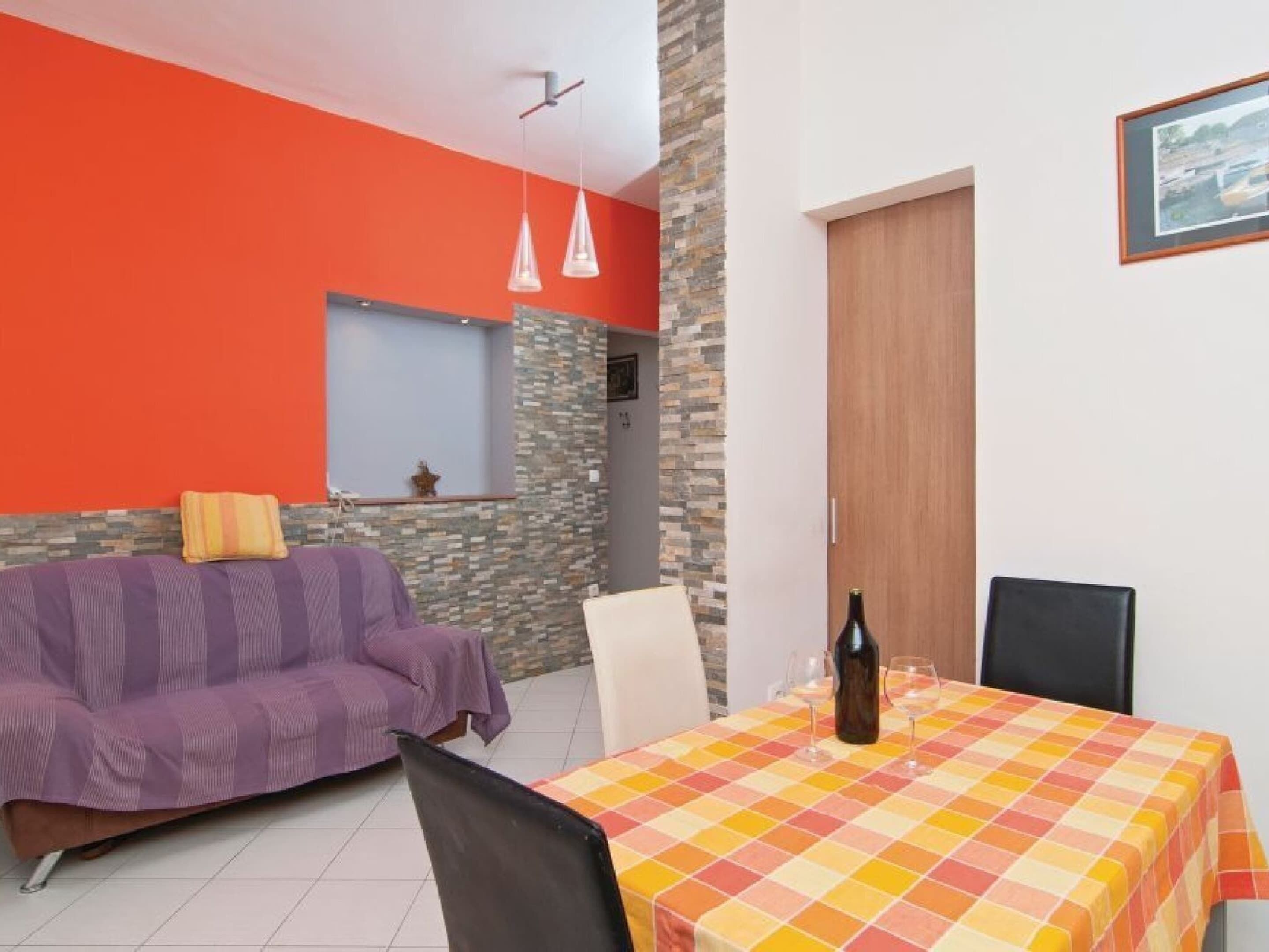 A dining area with a table set for two, a purple sofa, and a stone accent wall.