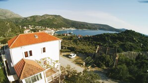 A white building with a red-tiled roof, a paved driveway, and a white car parked in front. - Apartments Baldo - Two Bedroom Apartment With Sea View (Dubrovacko Primorje)