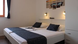 A double bed with a dark patterned bedspread, two pillows, a bedside table with a book and glasses, and a wall-mounted light fixture. - Apartments Baldo - Two Bedroom Apartment With Sea View (Dubrovacko Primorje)