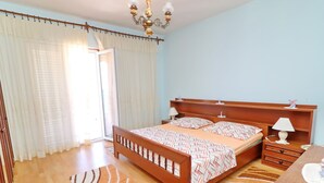 A bedroom with a wooden bed, a nightstand with a lamp, a wooden dresser, and a large window with curtains. - Apartments Peselj-three Bedroom Apartment With Terrace and Sea View (Smokvica)
