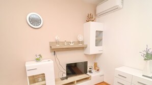 A modern, compact living space with a TV on a wooden stand, a small white cabinet, a clock on the wall, and a shelf with decorative items. - Apartments Peselj-three Bedroom Apartment With Terrace and Sea View (Smokvica)