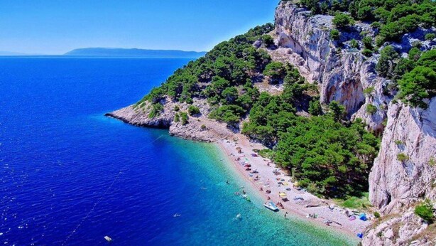 Una spiaggia costiera con acque blu cristalline, una scogliera rocciosa e una vegetazione lussureggiante.