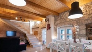 Un interno accogliente con una scala, soffitto in legno, pareti in pietra, un'area pranzo con tovaglioli fiorati e un televisore a sinistra.