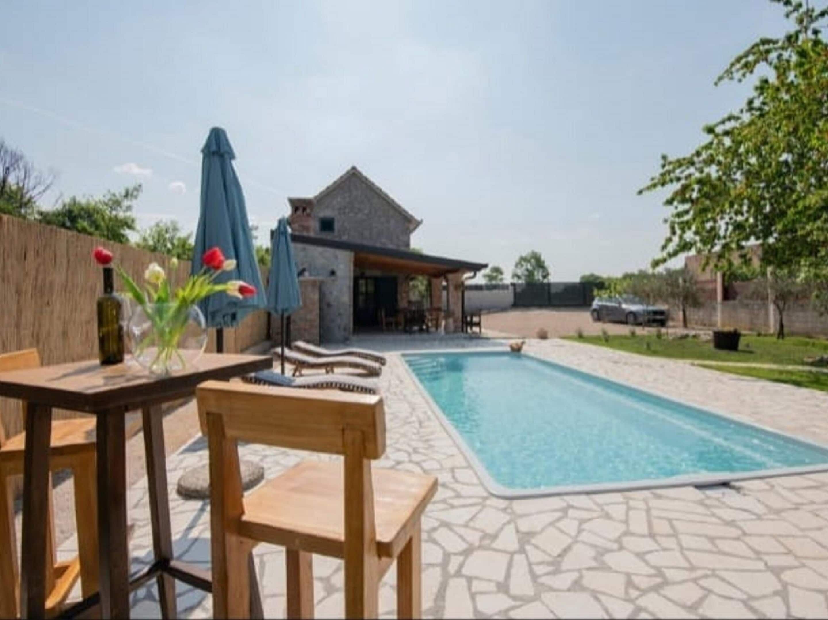 Une piscine avec des chaises longues et des parasols, une terrasse en pierre et un bâtiment en pierre en arrière-plan.