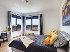 Ett modernt sovrum med en stor säng, ett skrivbord och utsikt över landsbygden.