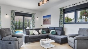 A modern living room with a sectional sofa, two armchairs, a coffee table, and large windows offering a view of the outdoors.