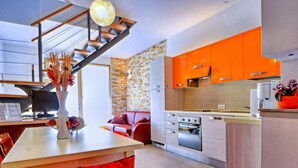 Une cuisine moderne avec des meubles de couleur orange, un four encastré et un coin repas agrémenté d’une chaise rouge.