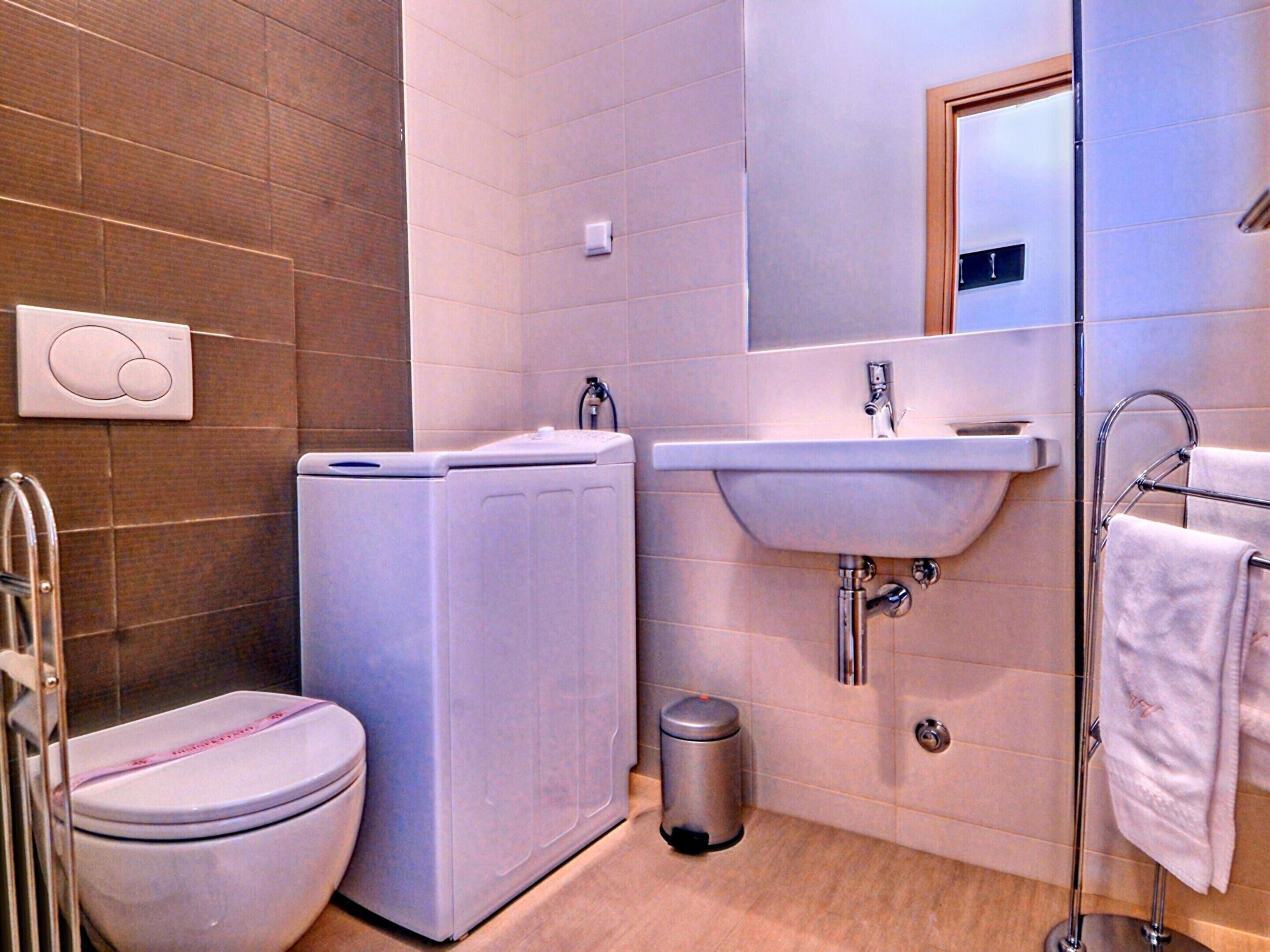 Ein modernes Badezimmer mit Toilette, Waschmaschine, Waschbecken und Handtuchhalter.