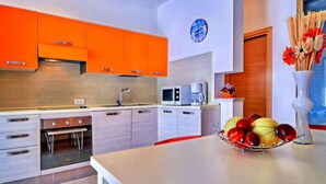 Une cuisine moderne avec des meubles de couleur orange, des appareils en acier inoxydable, un four à micro-ondes et un panier de fruits posé sur le plan de travail.