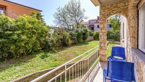 Un balcon doté de murs en pierre et d’une rambarde en métal, donnant sur un espace verdoyant agrémenté d’arbustes et d’un arbre.